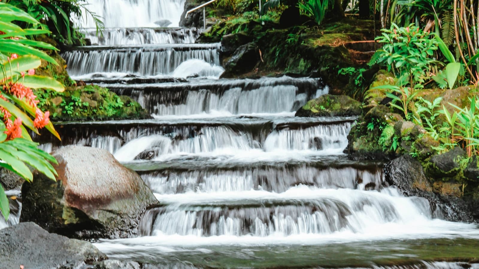Cascading hot springs waterfall at a La Fortuna family resort, surrounded by tropical rainforest β the signature Arenal hotel experience